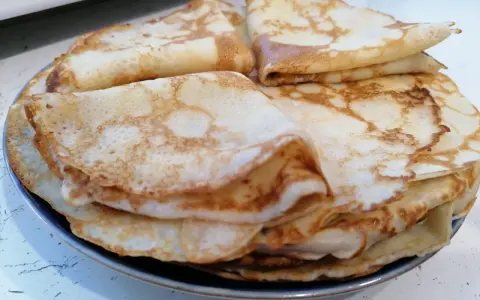 Stos cienkich, złocistych naleśników, idealnych na śniadanie lub deser. Każdy z nich ma delikatne pęcherzyki i lekko przypieczone brzegi.