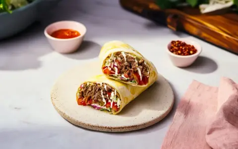 Pyszny rollo z mięsem, warzywami i sosem, podany na talerzu. Obok miseczki z sosem i papryczkami chili.