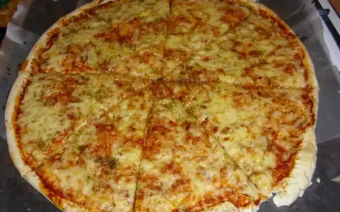 Pyszna pizza margerita z ciągnącym się serem i aromatycznymi ziołami, pokrojona na 8 kawałków.