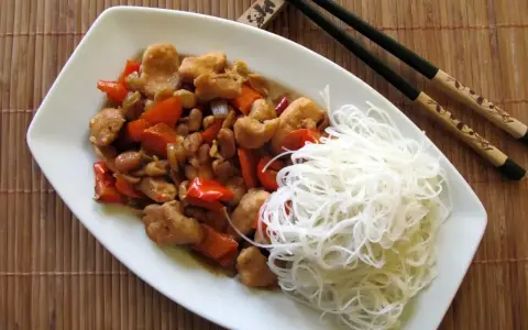 Kurczak kung pao po seczuańsku z orzeszkami ziemnymi i papryką, podany z ryżowym makaronem.