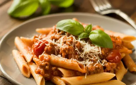 Penne z sosem bolognese, posypane parmezanem i udekorowane bazylią. Pyszne potrawy włoskie na talerzu.