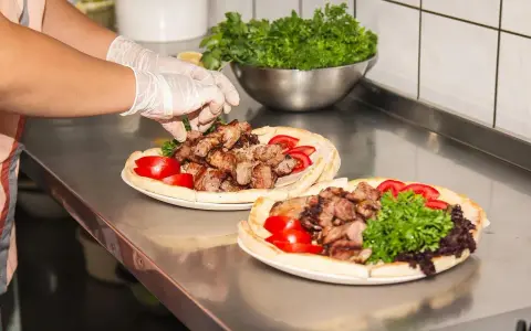 Ręce w rękawiczkach układają mięso na plackach z pomidorami i zieloną sałatą. Pyszny kebab gemuse gotowy do podania.