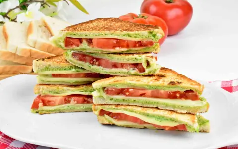 Pyszne włoskie kanapki z pomidorami i zielonym pesto, ułożone na talerzu. Idealne na lekki posiłek.