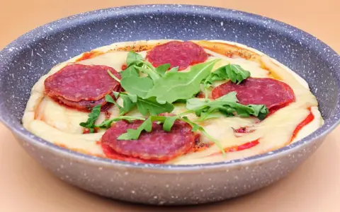Mini pizza na patelni z serem, rukolą i plasterkami pikantnej salsiccii.