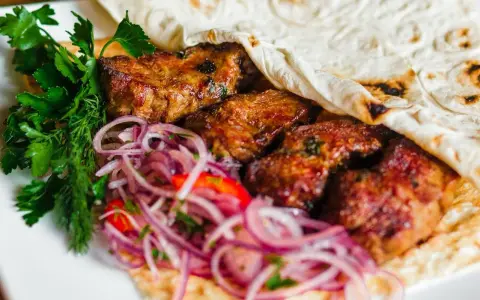 Pyszne mezze: soczyste mięso zawinięte w placek, z dodatkiem świeżej natki i czerwonej cebuli. Idealne na przekąskę.