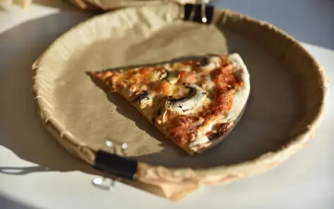 Kawałek pizzy z pieczarkami na papierowym talerzu. Zastanawiasz się, ile kalorii ma pizza?
