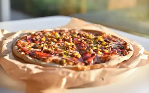 Apetyczna pizza Guiseppe 4 sery, z widocznymi kawałkami mięsa, kukurydzy i papryki, leży na papierze do pieczenia.