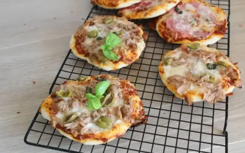 Kilka pysznych pizzett z tuńczykiem, oliwkami i bazylią na czarnej kratce.