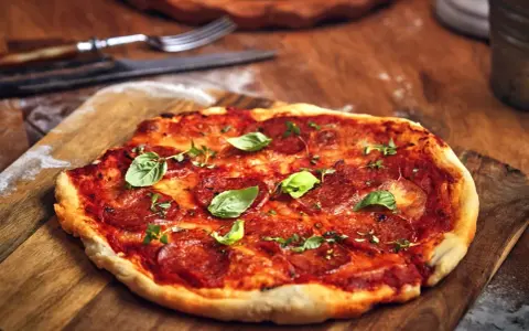 Pikantna spianata calabrese na pizzy, ozdobiona świeżą bazylią i ziołami, czeka na talerzu.