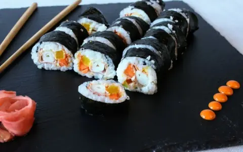 Rząd hosomaki surimi z marchewką i żółtą papryką, podane z imbirem i pomarańczowym sosem.
