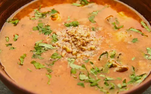 Aromatic gruzińska zupa charczo w glinianej misce, ozdobiona posiekanymi orzechami i świeżą kolendrą.
