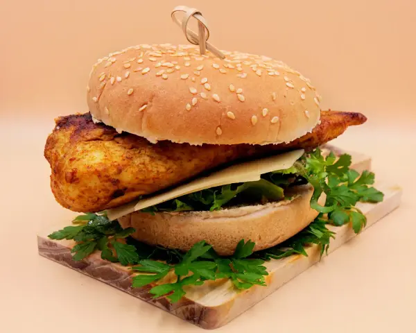 Pikantny kurczakburger z serem i świeżą sałatą, podany na desce z natką pietruszki.
