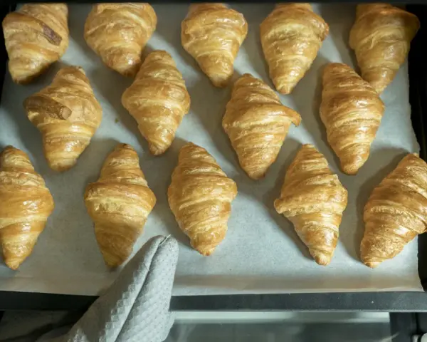 Pyszne, złociste croissanty ułożone na blasze. Idealne na śniadanie.