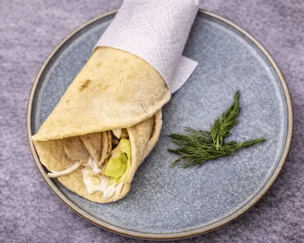 Pita co to? Sycący wrap z mięsem, warzywami i sosem, zawinięty w płaski chlebek, podany na talerzu z gałązką koperku.