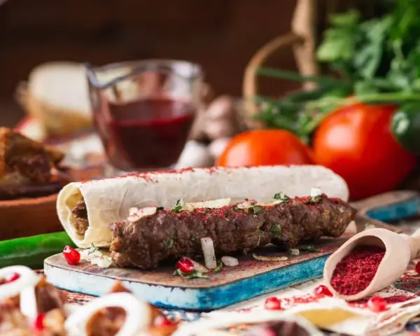 Pyszny gruziński kebab zawinięty w lawasz, posypany sumakiem i ziołami, z dodatkami warzyw i sosu.