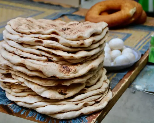 Stos świeżego, ciepłego ciasta na kebab, obok miseczka jajek i okrągły chleb.
