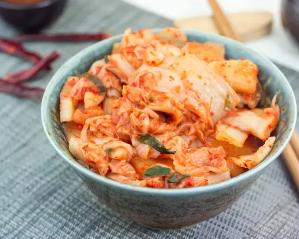 Misternie przygotowane kimchi, czyli co to jest? Pikantna, fermentowana kapusta pekińska w misce, obok pałeczki i suszone papryczki chili.