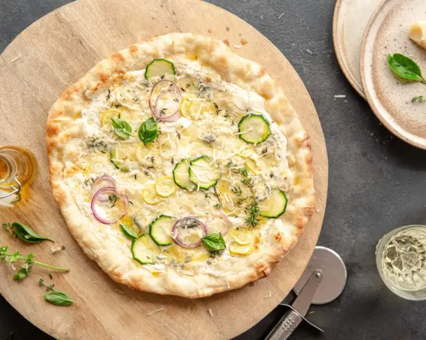 Pyszna pizza bianca z cukinią, cebulą i cytryną, posypana parmezanem i ziołami. Idealna na letni wieczór.