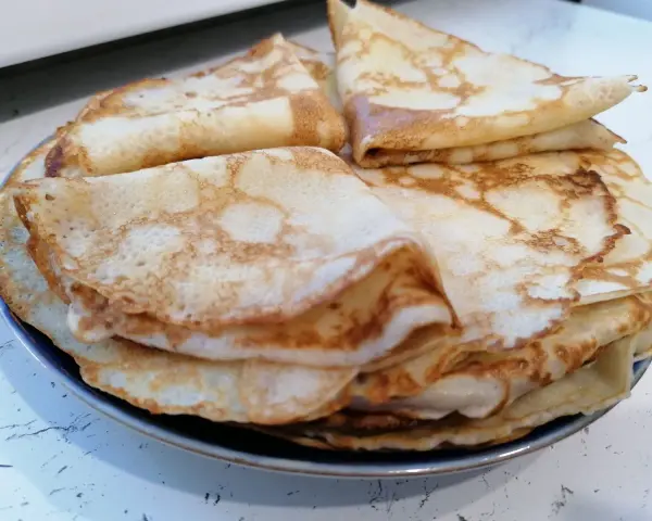 Stos cienkich, złocistych naleśników, idealnych na śniadanie lub deser. Każdy z nich ma delikatne pęcherzyki i lekko przypieczone brzegi.