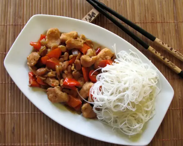 Kurczak kung pao po seczuańsku z orzeszkami ziemnymi i papryką, podany z ryżowym makaronem.