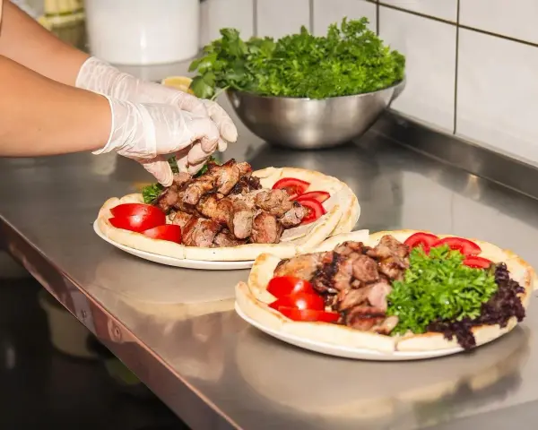 Ręce w rękawiczkach układają mięso na plackach z pomidorami i zieloną sałatą. Pyszny kebab gemuse gotowy do podania.