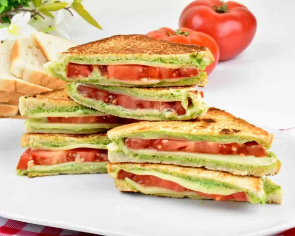 Pyszne włoskie kanapki z pomidorami i zielonym pesto, ułożone na talerzu. Idealne na lekki posiłek.