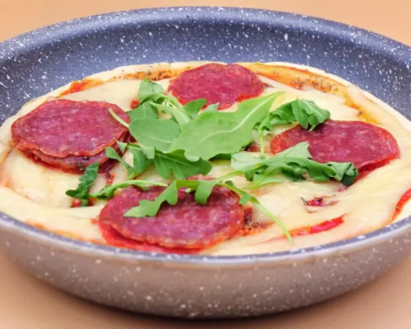 Mini pizza na patelni z serem, rukolą i plasterkami pikantnej salsiccii.