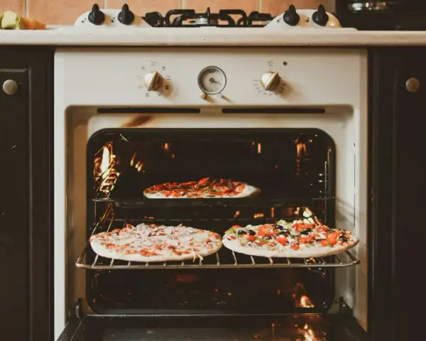 Trzy pizze pieką się w piekarniku z termoobiegiem. Jedna na górnej półce, dwie na dolnej.