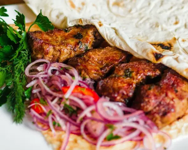 Pyszne mezze: soczyste mięso zawinięte w placek, z dodatkiem świeżej natki i czerwonej cebuli. Idealne na przekąskę.