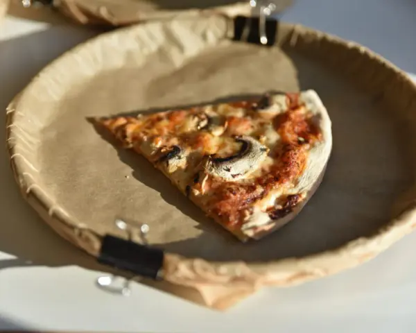 Kawałek pizzy z pieczarkami na papierowym talerzu. Zastanawiasz się, ile kalorii ma pizza?