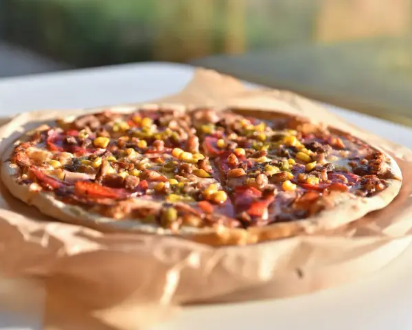 Apetyczna pizza Guiseppe 4 sery, z widocznymi kawałkami mięsa, kukurydzy i papryki, leży na papierze do pieczenia.