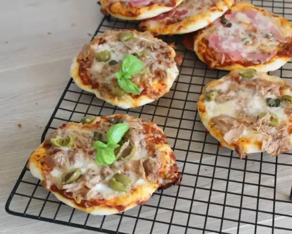 Kilka pysznych pizzett z tuńczykiem, oliwkami i bazylią na czarnej kratce.