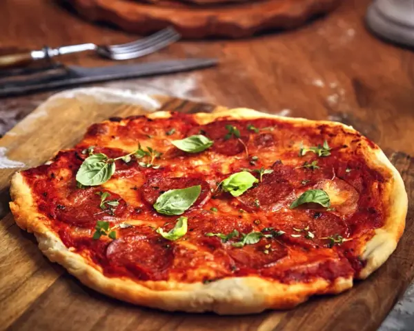 Pikantna spianata calabrese na pizzy, ozdobiona świeżą bazylią i ziołami, czeka na talerzu.