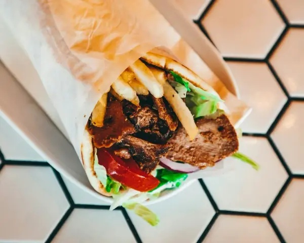 Pyszny kebab z mięsem, frytkami, warzywami i sosem. Zastanawiasz się, ile kcal ma kebab? Ten wygląda na sycący!