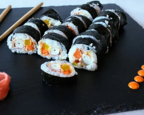 Rząd hosomaki surimi z marchewką i żółtą papryką, podane z imbirem i pomarańczowym sosem.