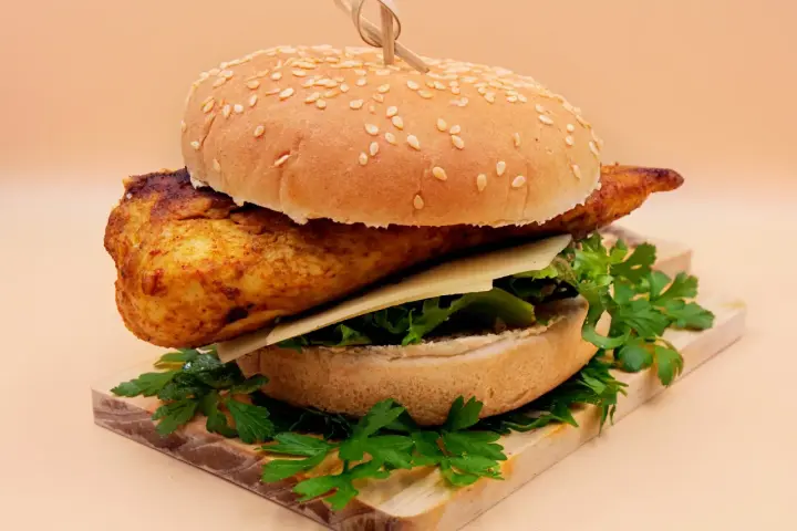 Pikantny kurczakburger z serem i świeżą sałatą, podany na desce z natką pietruszki.