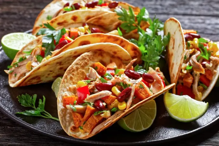 Pyszne meksykańskie jedzenie: tacos z kurczakiem, fasolą, kukurydzą i papryką, podane z limonką i kolendrą.