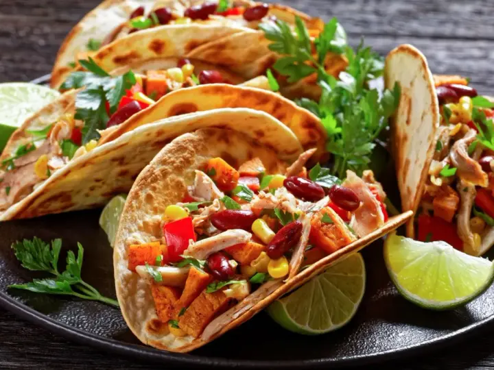 Pyszne meksykańskie jedzenie: tacos z kurczakiem, fasolą, kukurydzą i papryką, podane z limonką i kolendrą.