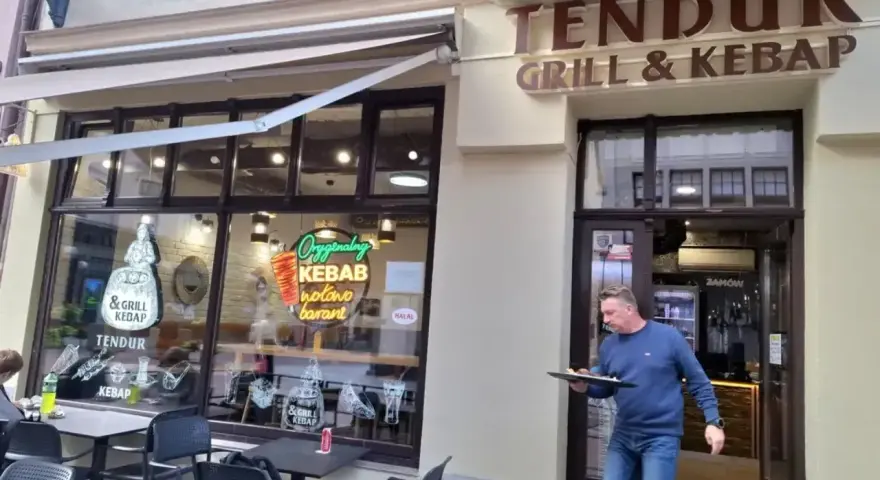 Mężczyzna wychodzi z lokalu "Tendur Grill & Kebap", niosąc talerz. W witrynie neonowy napis "Oryginalny Kebab".