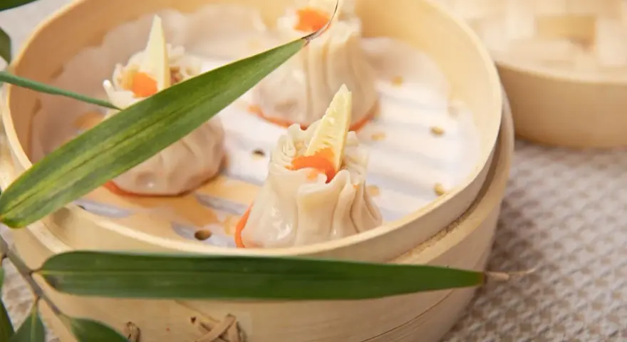 Pierożki dim sum w bambusowym parowniku, ozdobione kawałkiem bambusa i pomarańczowym ikrą.