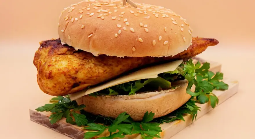 Pikantny kurczakburger z serem i świeżą sałatą, podany na desce z natką pietruszki.