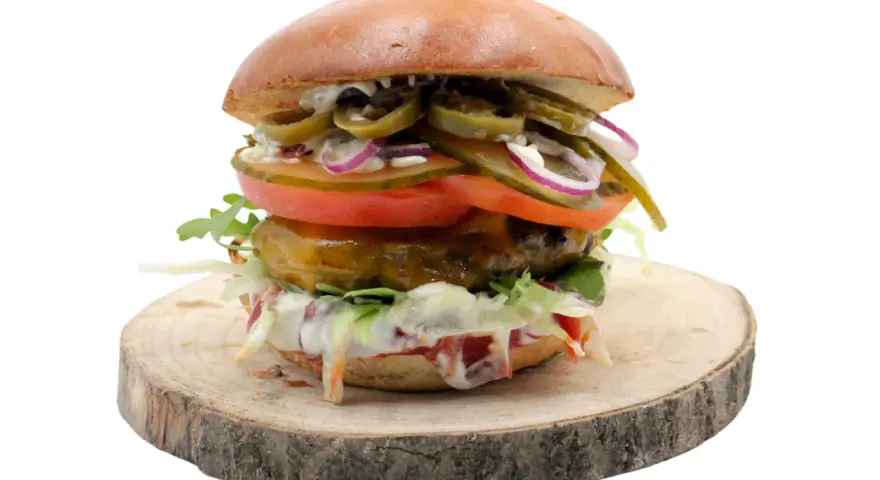Pikantny jalapeno burger z pomidorem, cebulą i sałatą na drewnianym krążku. Zastanawiasz się nad jego kcal?