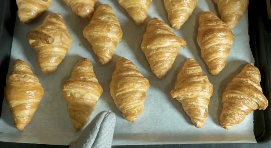 Pyszne, złociste croissanty ułożone na blasze. Idealne na śniadanie.