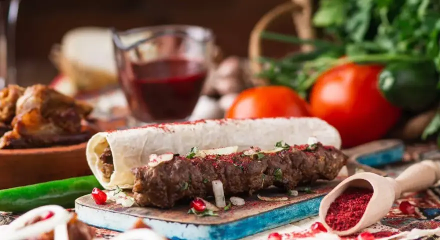 Pyszny gruziński kebab zawinięty w lawasz, posypany sumakiem i ziołami, z dodatkami warzyw i sosu.