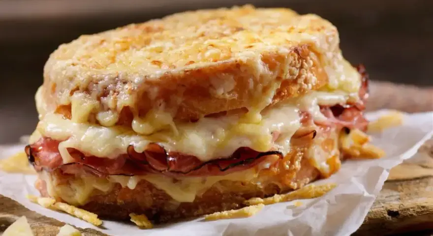 Pyszny croque madame z rozpływającym się serem i szynką, podany na papierze na drewnianej desce.