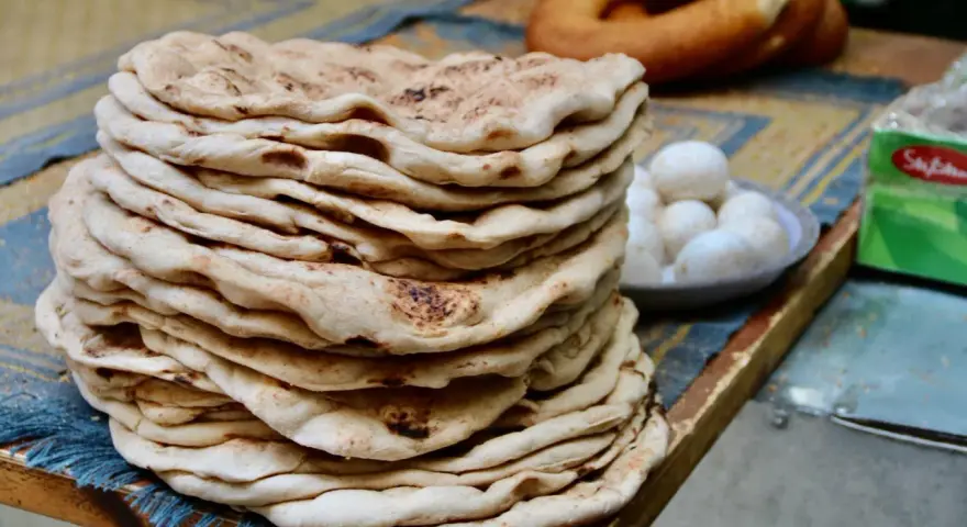 Stos świeżego, ciepłego ciasta na kebab, obok miseczka jajek i okrągły chleb.