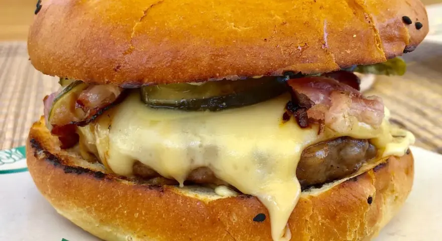 Pyszny burger z dzika z rozpływającym się serem, chrupiącym boczkiem i piklami. Idealny na leśną ucztę!