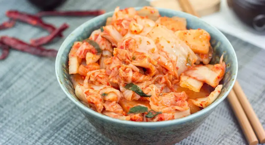 Misternie przygotowane kimchi, czyli co to jest? Pikantna, fermentowana kapusta pekińska w misce, obok pałeczki i suszone papryczki chili.