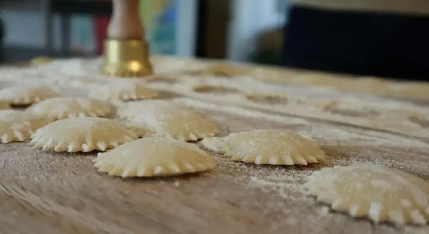 Świeże ravioli na drewnianej desce, posypane mąką. Zastanawiasz się, ravioli z czym podawać?
