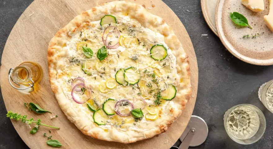 Pyszna pizza bianca z cukinią, cebulą i cytryną, posypana parmezanem i ziołami. Idealna na letni wieczór.